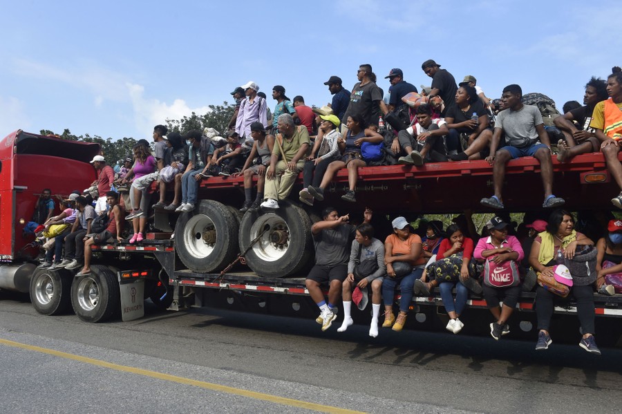 Dozens of people ride on the back of a semi-trailer truck.