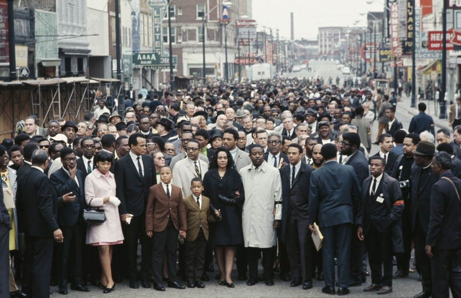 A large crowd of people stands in a street, behind Coretta Scott King.
