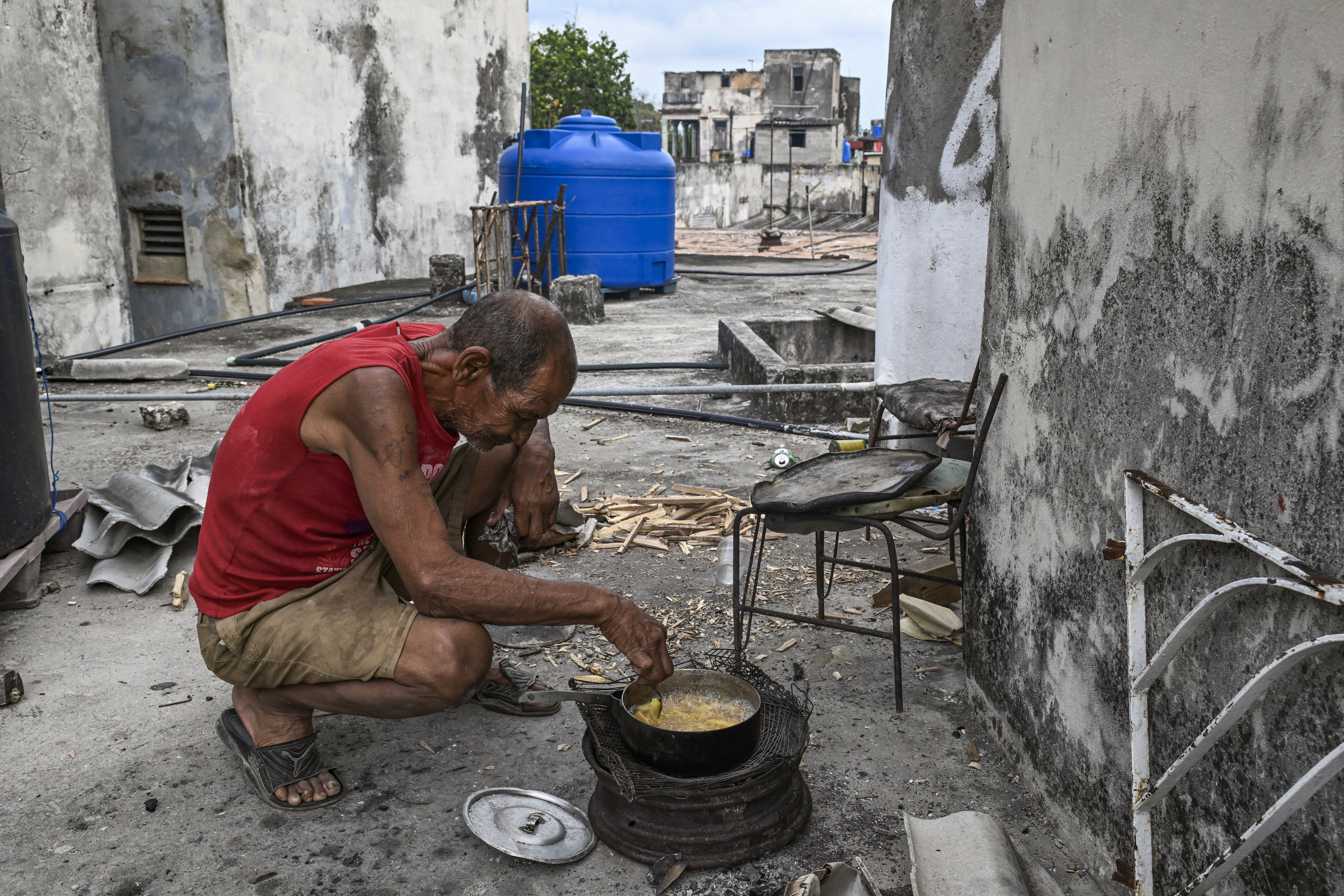 A man kneels, cooking with firewood over a makeshift stove.