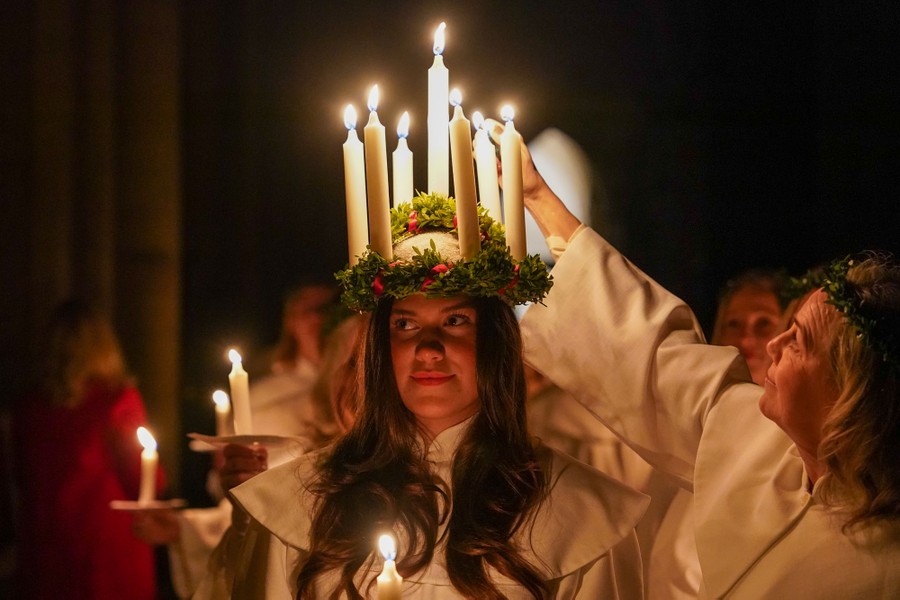A young woman wears a headdress adorned with large candles, which are being lit before a procession.