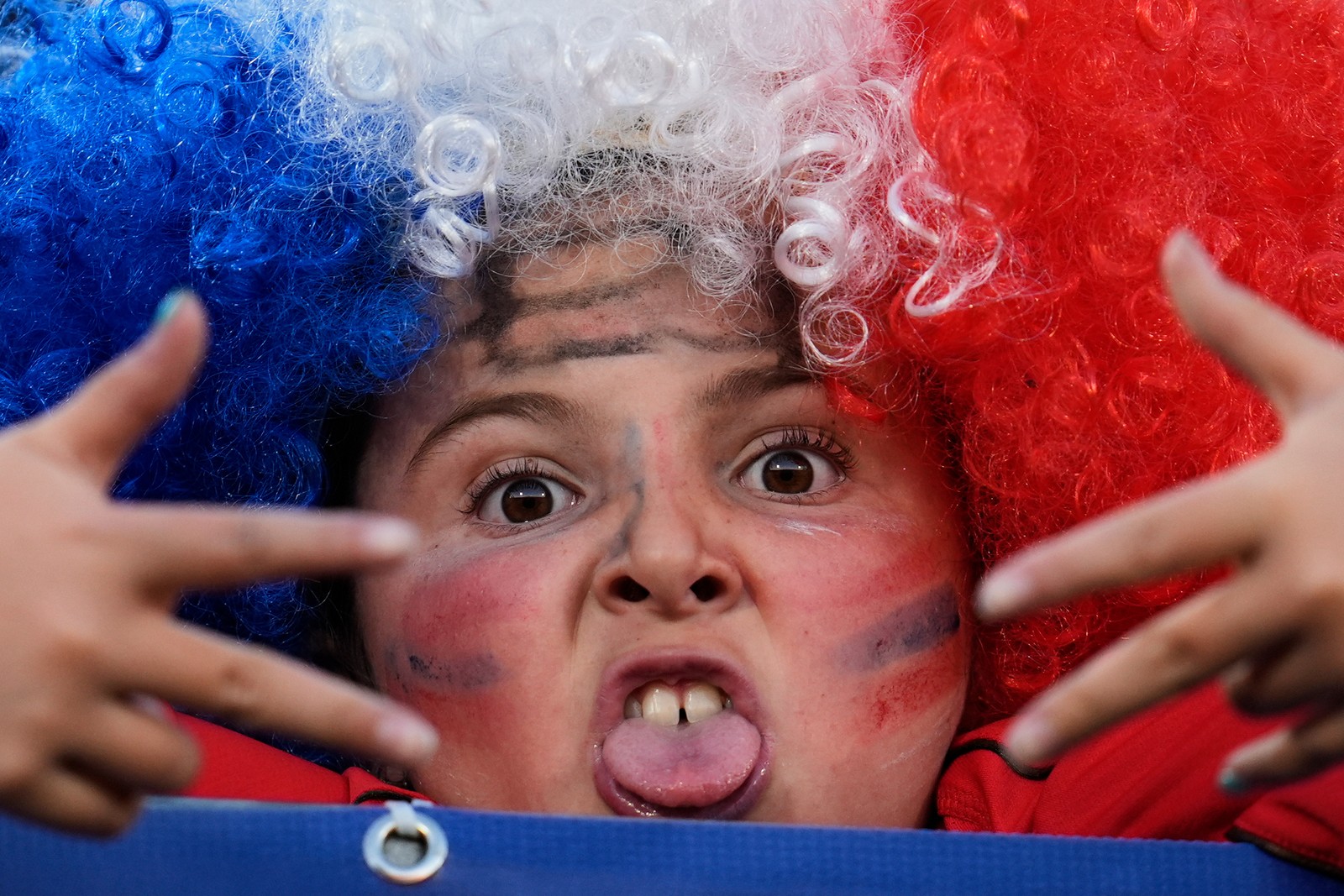 A young soccer fan wearing a blue-white-and-red wig makes a face at the camera.