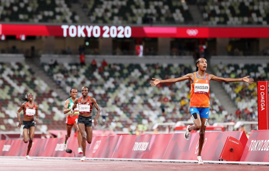 Runners cross a finish line and react in a largely-empty stadium.