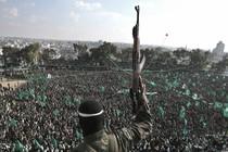 A militant, photographed from behind, holds a gun in the air as he stands before a crowd waving green flags