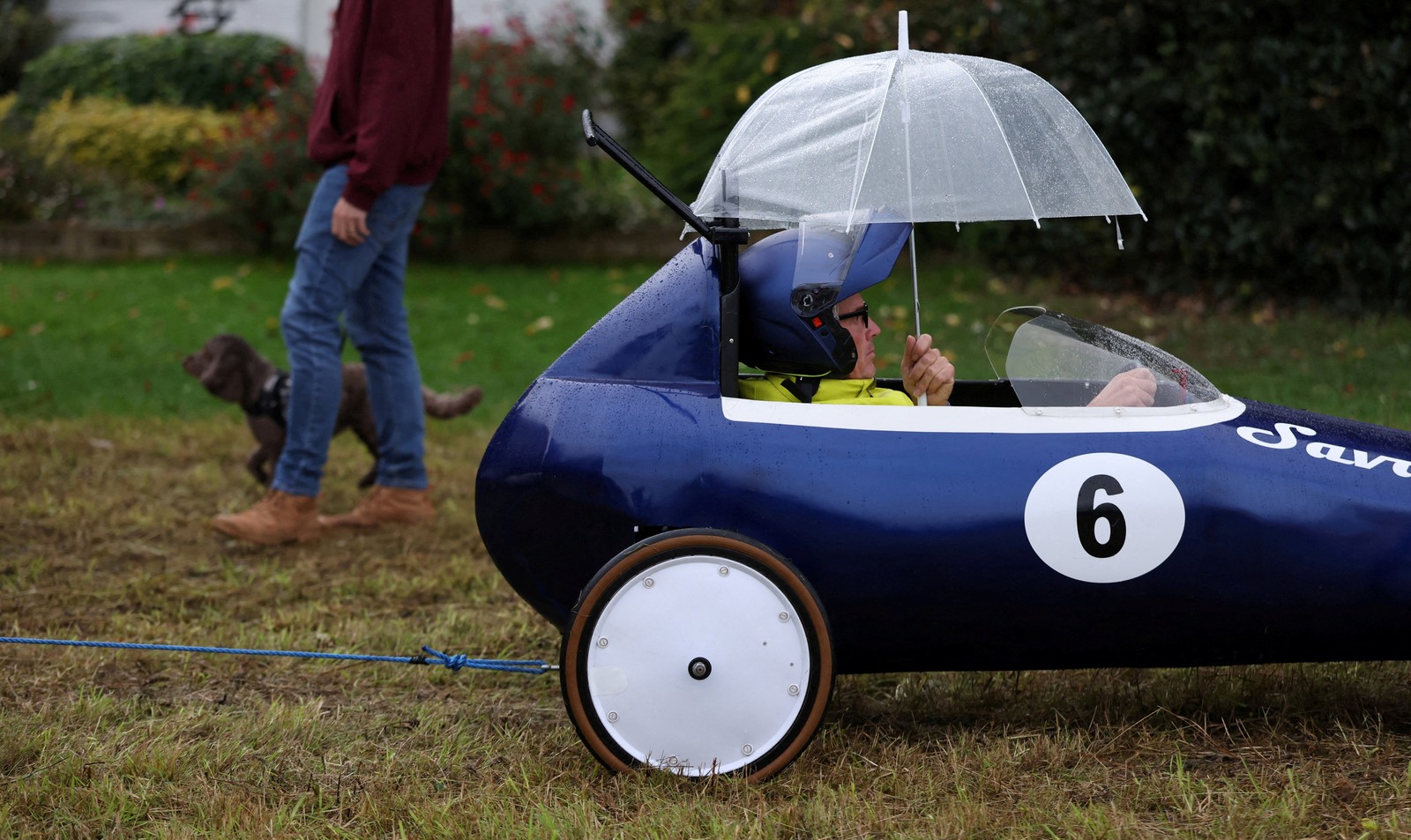 A driver sits in a small racing cart, holding an umbrella above their head.