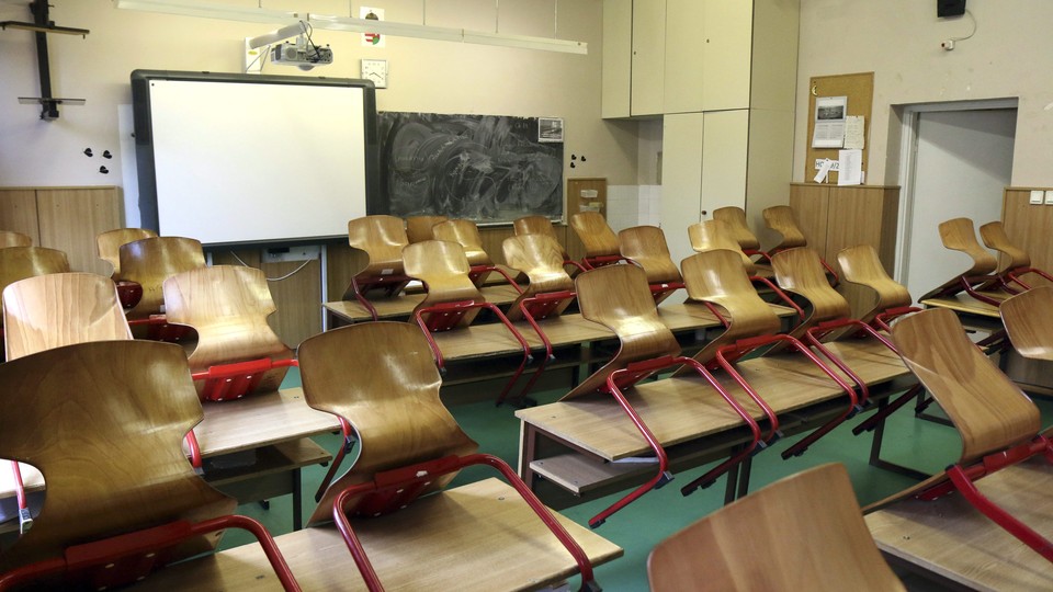 An empty classroom. All the chairs are on top of the desks. There is a Smartboard at the front of the room.