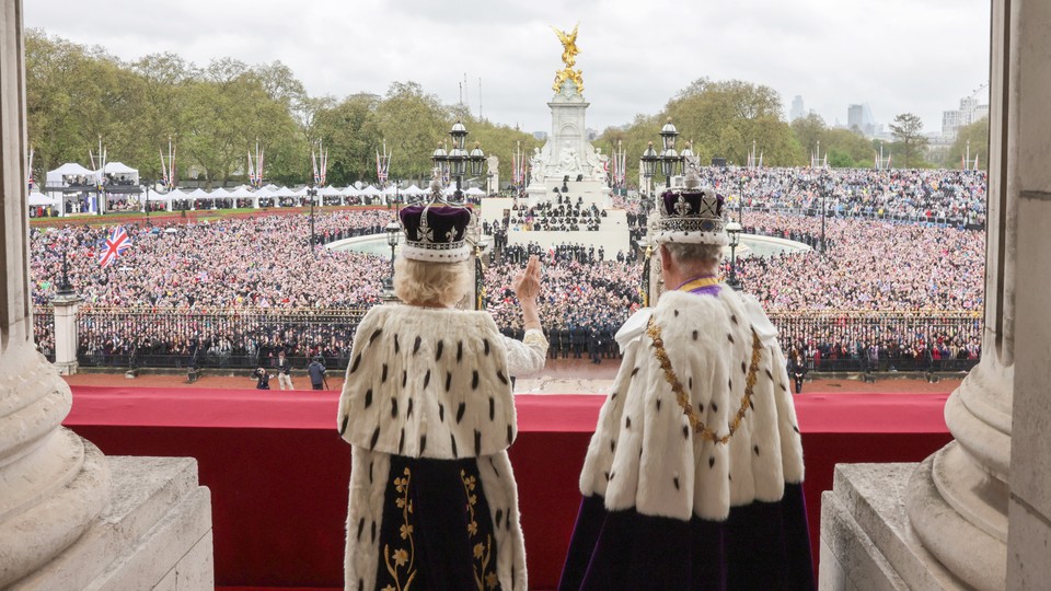 King Charles and Queen Camilla stand on the balcony at Buckingham Palace with their backs to the camera, facing the crowds at their coronation