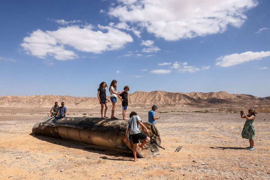 People stand on top of the remains of a large missile in a desert.