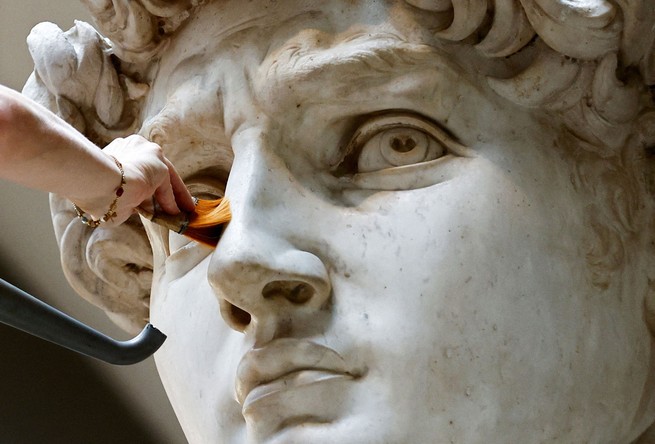 The restorer Eleonora Pucci cleans dust and debris off Michelangelo’s statue of David using a backpack vacuum and synthetic fiber brush.