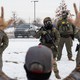A man standing with his hands up opposite a group of heavily armed ICE agents