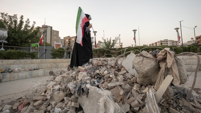 A veiled Iranian art student holds a country flag while standing on symbolic debris of a destroyed building as she performs in an anti-war conceptual play at a square in downtown Tehran, Iran
