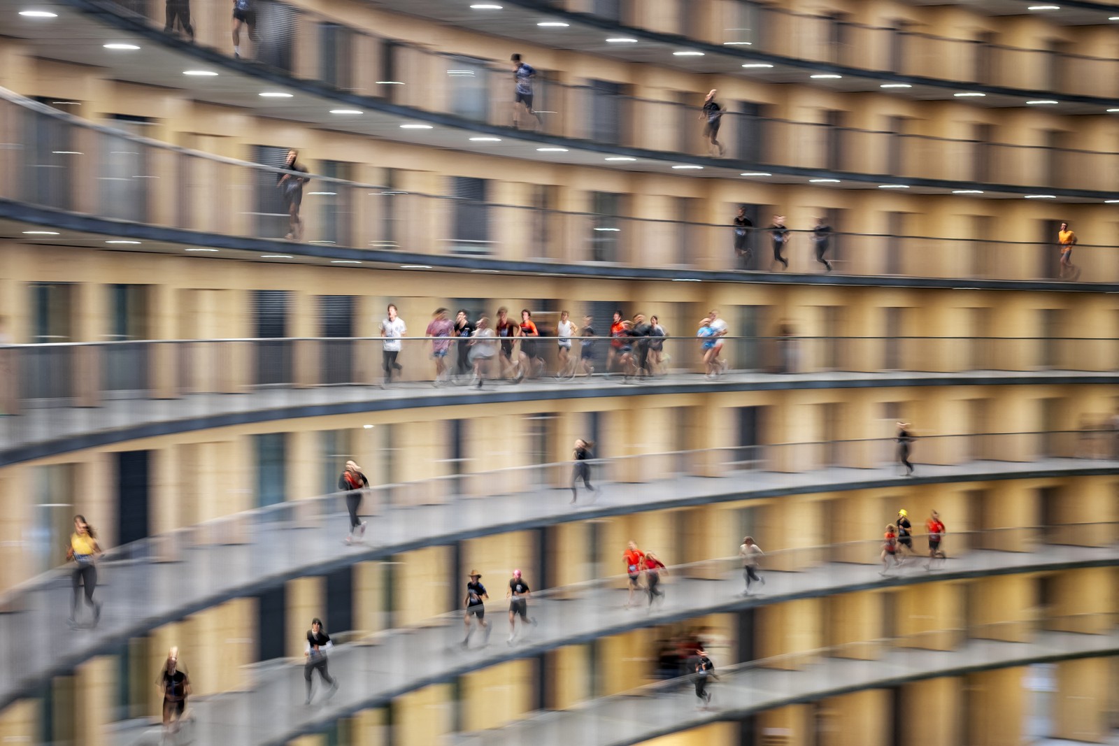 A slightly motion-blurred image of many students running along several curved balcony walkways.