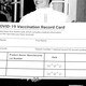 Three well-dressed people hold an enormous, fake COVID-19 vaccination card.