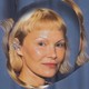 Pamela Anderson wearing an elaborate earring and matching blueish dress in front of a distorted outline of her image in front of a blue curtain