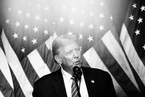 Donald Trump stands at a microphone in front of American flags.