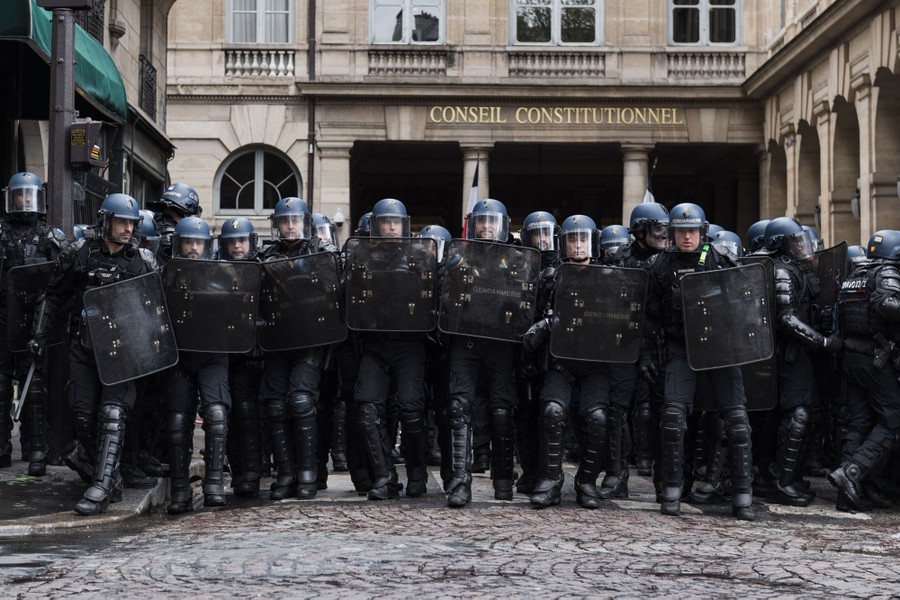 A line of riot police stands in the middle of a street.