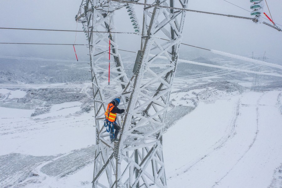 A worker removes ice from power lines high atop a tall transmission tower.