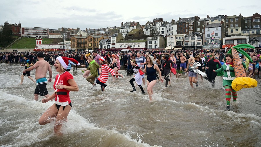 Dozens of costumed people run into the surf in a seaside town.