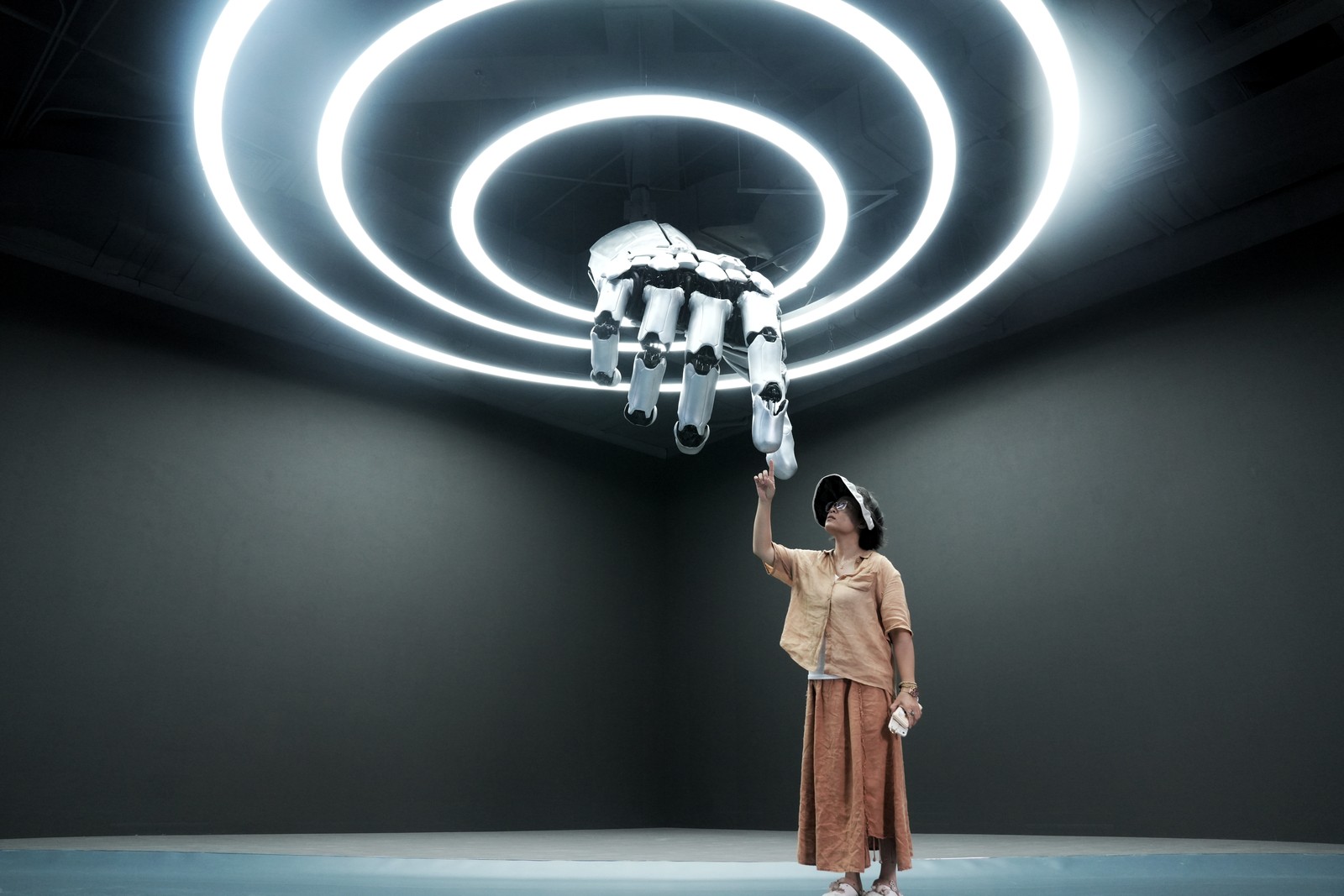 A person reaches up toward a sculpture of a large robotic hand coming out of the ceiling.