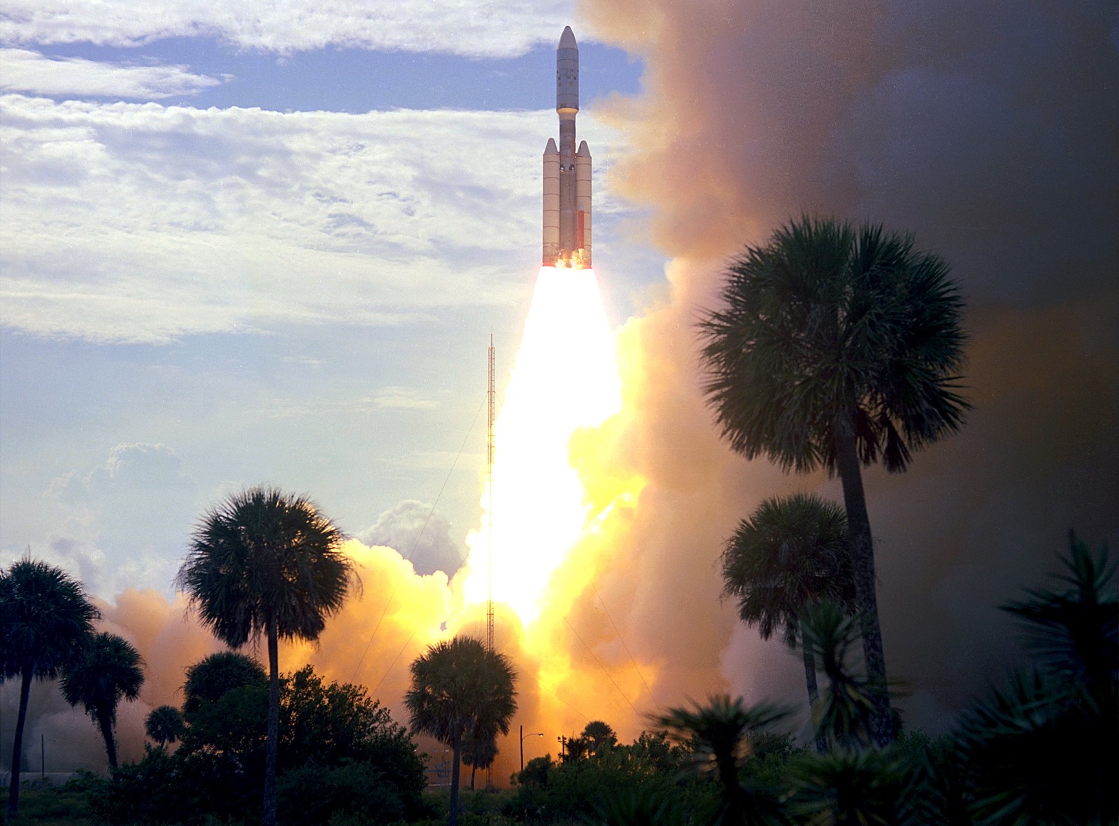 A rocket launch, with bright exhaust flames seen past palm trees