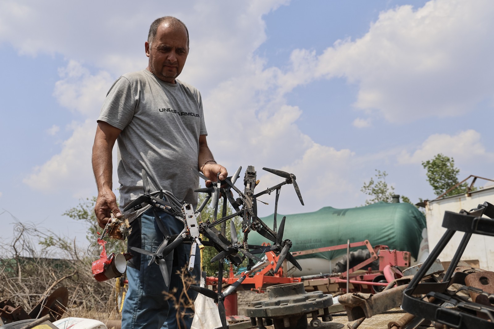 A farmer holds up several wrecked small drones.