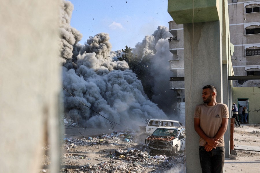 A man takes cover behind a column as an explosion blasts dust and debris from a nearby building.
