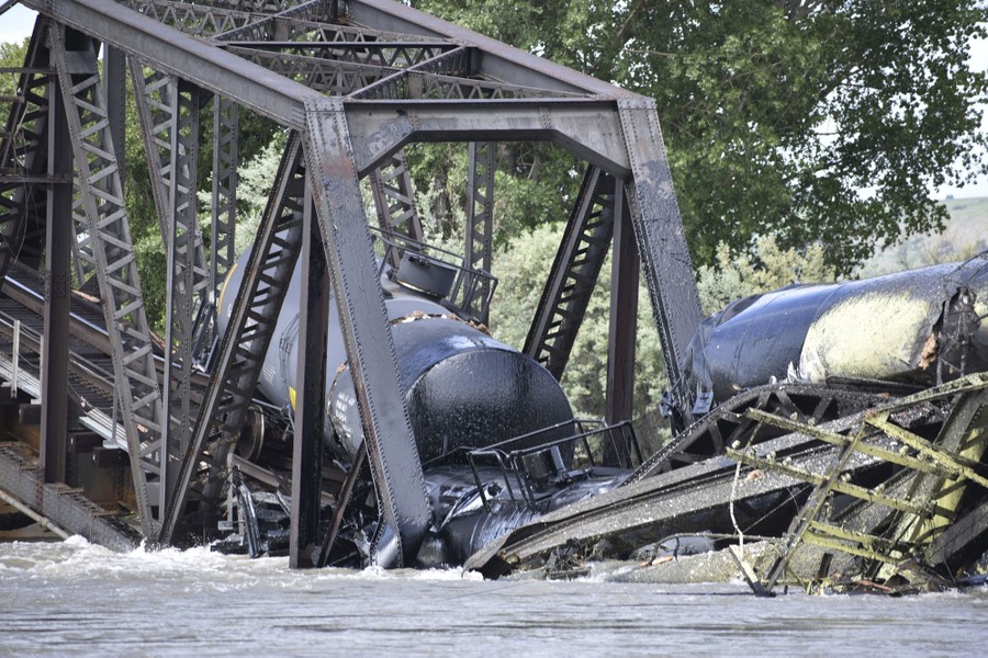 Several damaged rail cars sit on a collapsed railroad bridge in a river.
