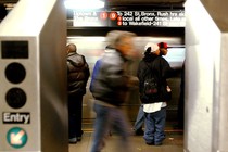 People standing on a subway platform in New York City, framed by two turnstiles