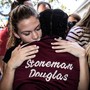Young people hug. One is wearing a jacket that says "Stoneman Douglas" on the back.