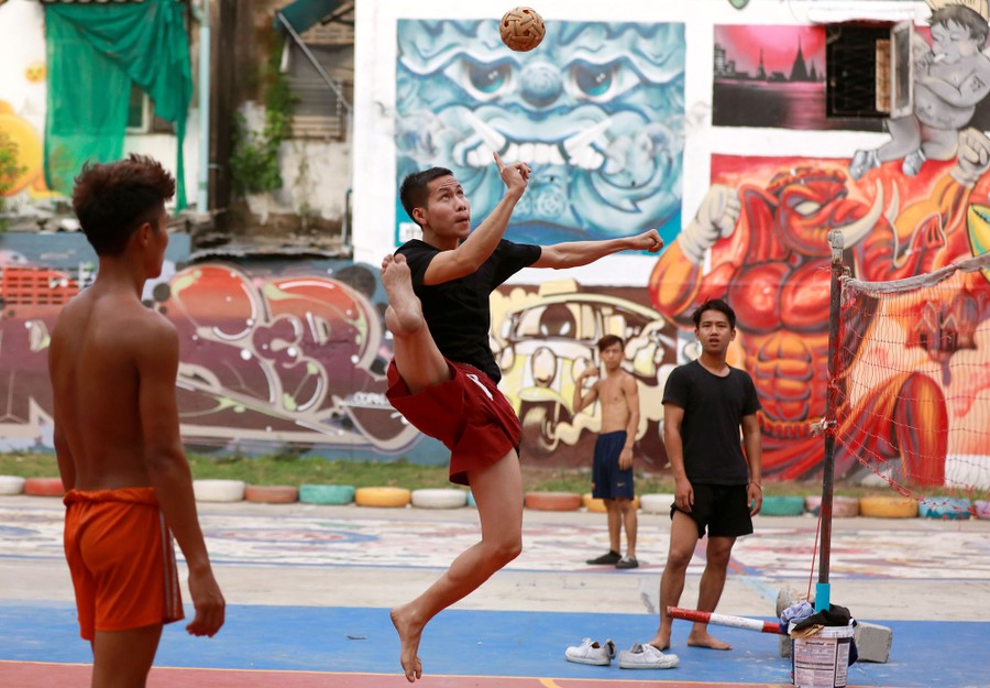 Several men kick a ball over a net at an informal outdoor court.
