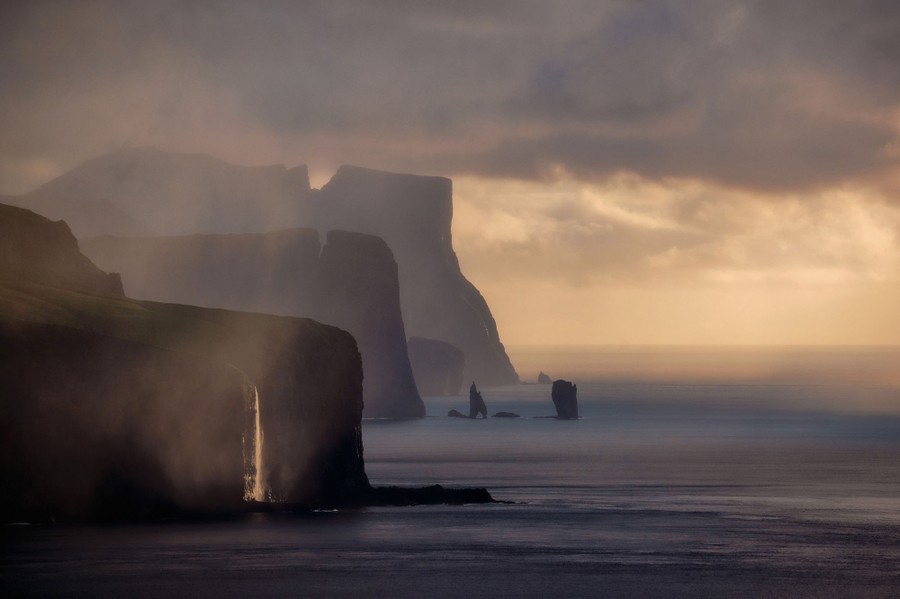 A view of seaside cliffs and a waterfall under low clouds