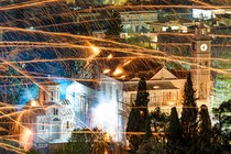 Streaks of sparks left by handmade rockets criss-cross over buildings in an old village center in Greece.