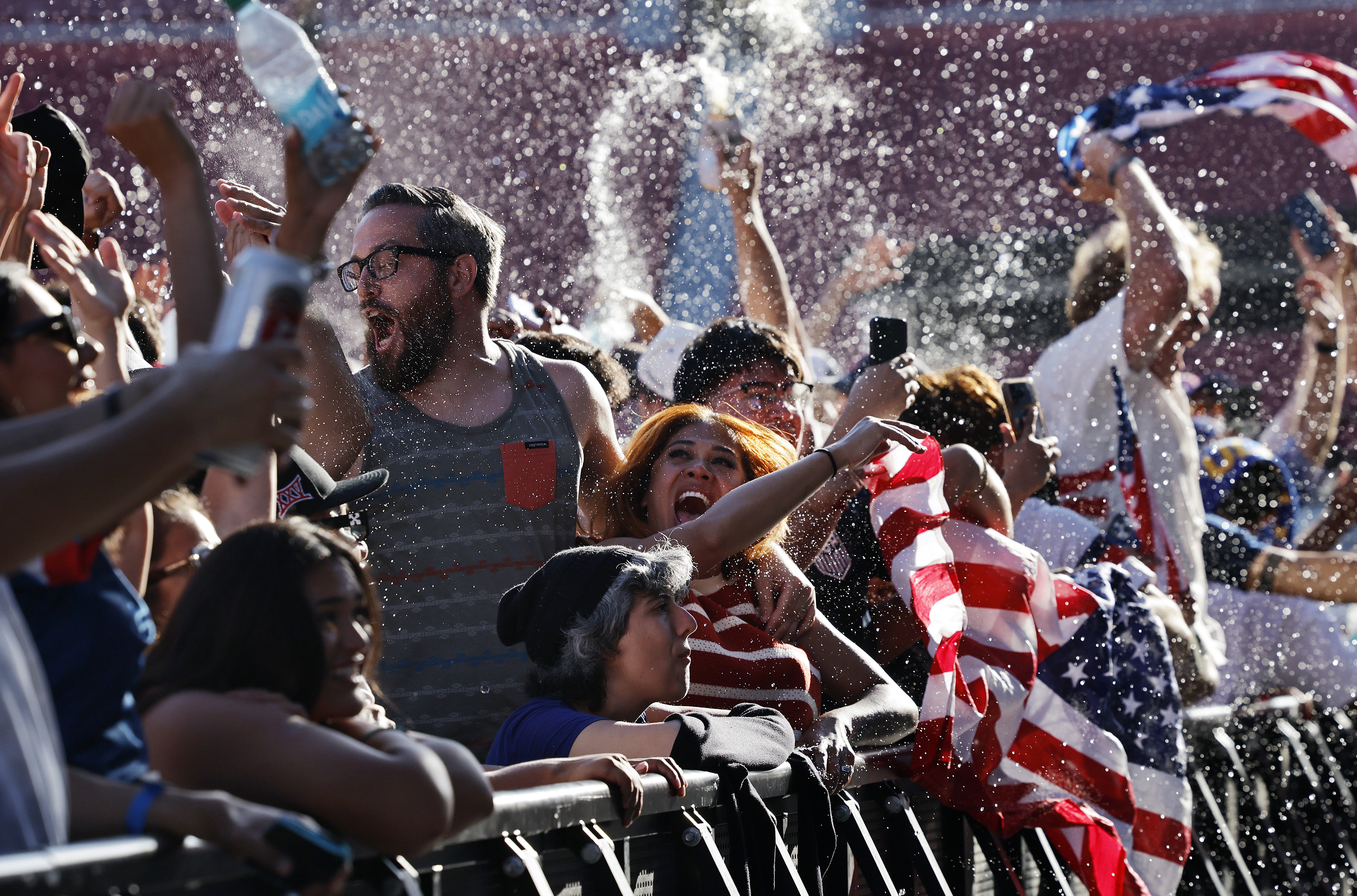 Team USA fans cheer and celebrate, throwing water in the air and waving flags.