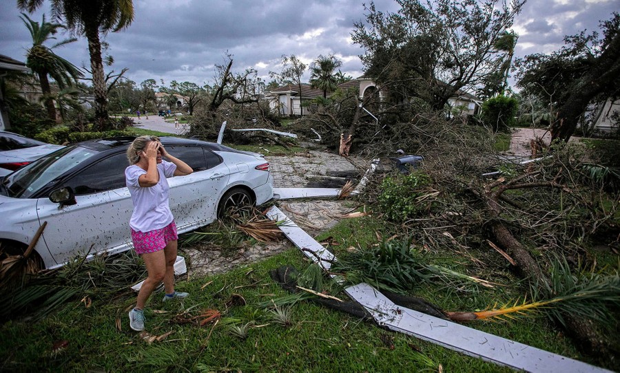 A person reacts, standing in a yard surrounded by piles of storm debris.
