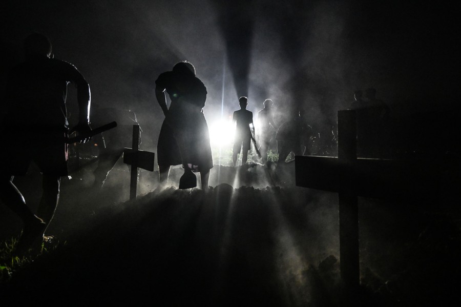 Several people dig in a graveyard, seen in silhouette at night.