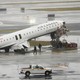 Photograph of the wreckage of Air Canada airplane on the runway of an airport, with the plane’s nose upturned with exposed wiring and torn metal exposing its inside