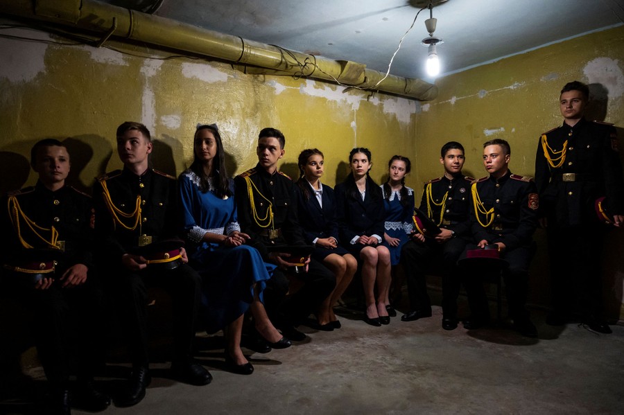 Students in military uniforms sit on a bench inside an underground shelter.
