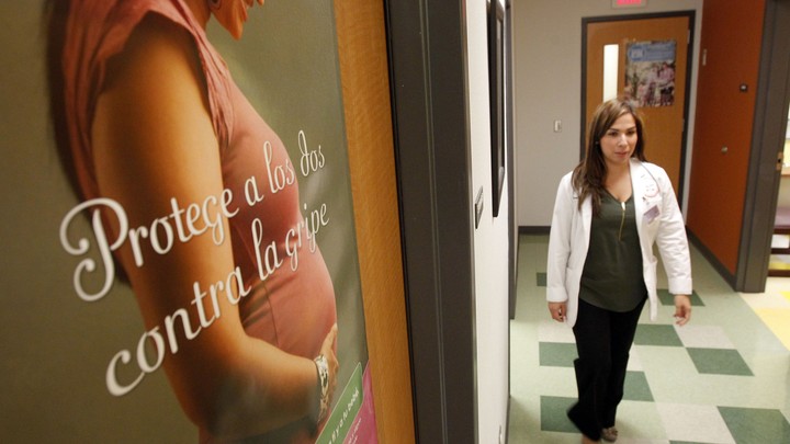 A woman walks through a clinic with a poster of a pregnant woman on the wall.