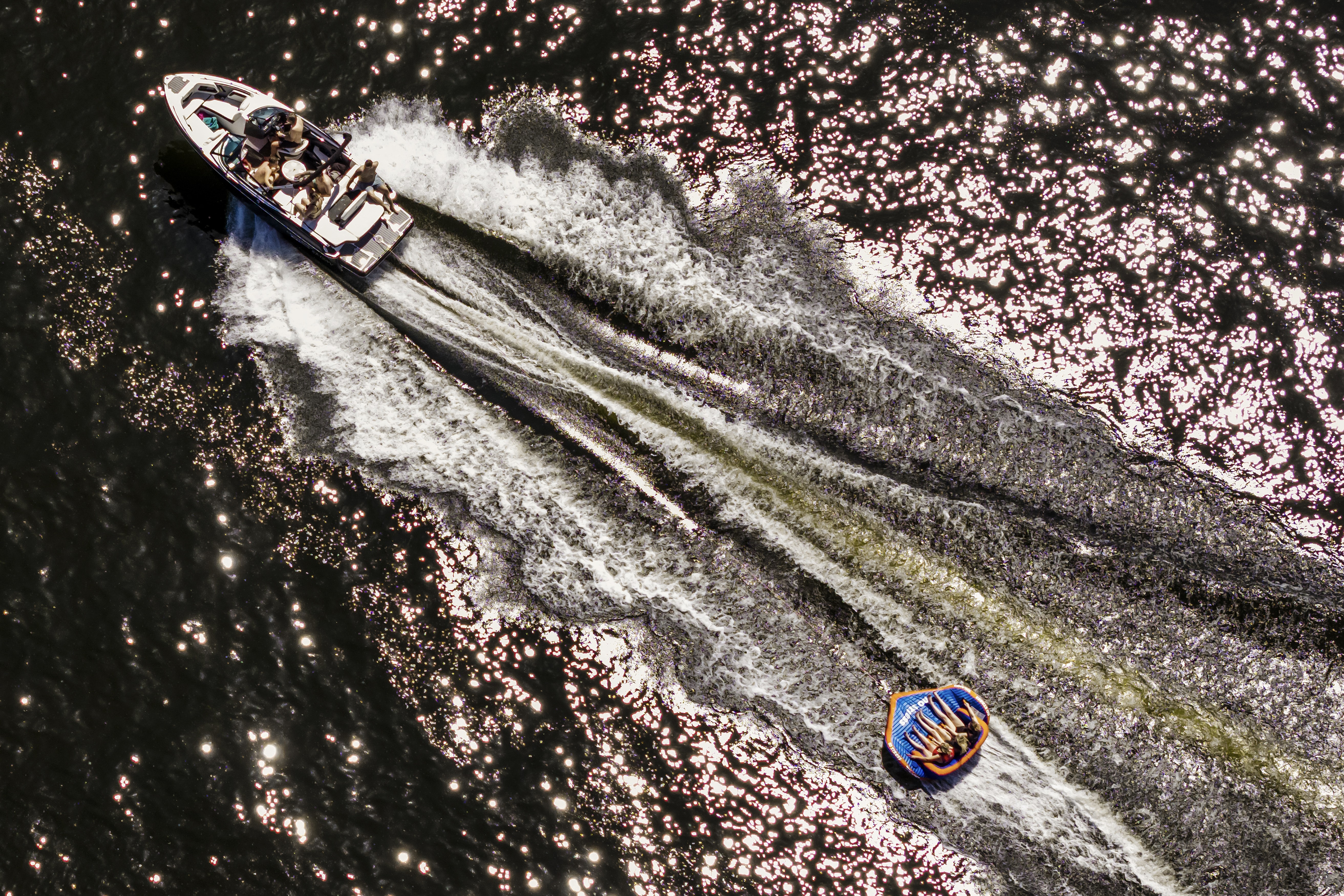 An aerial photograph of people being pulled on an inflatable raft by a motorboat on a lake
