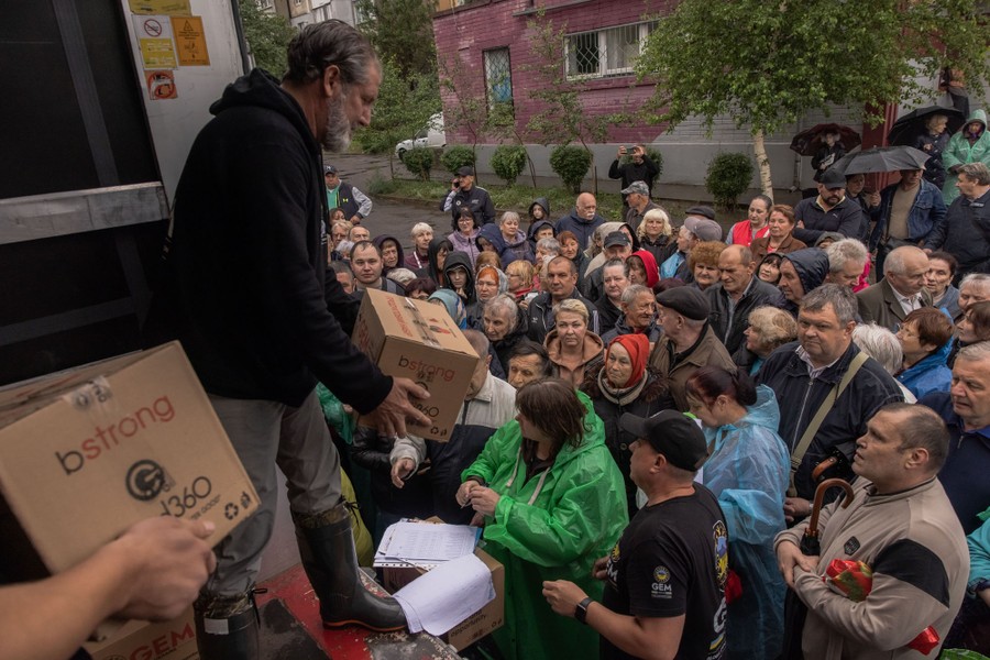 A crowd of people gathers around a truck, where people hand out boxes of aid.