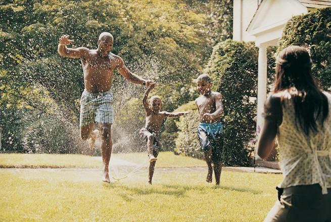 family frolicking on a lawn with a sprinkler