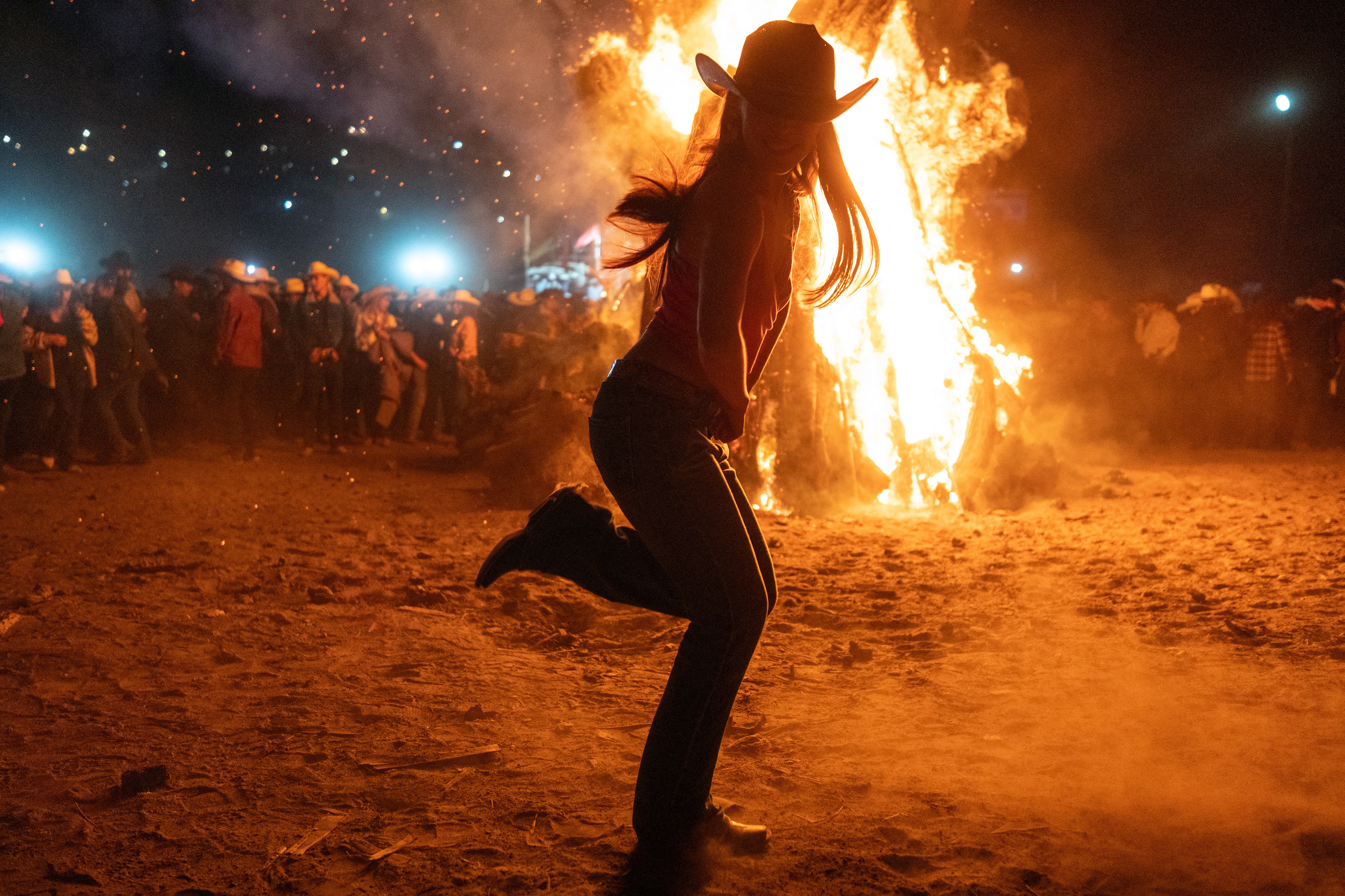 A woman wearing a cowboy hat dancing in front of a bonfire.