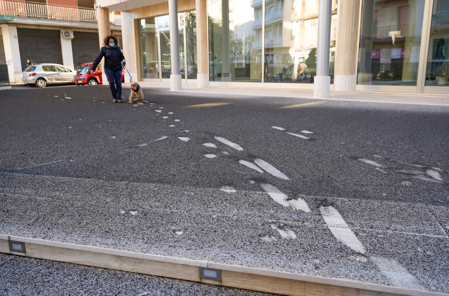 A person walks with a dog over a sidewalk covered with a thin layer of dark ash.