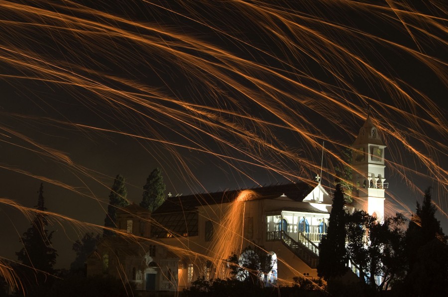 Firework rockets fall from the sky, leaving streaks of light, as at least one strikes a church building.