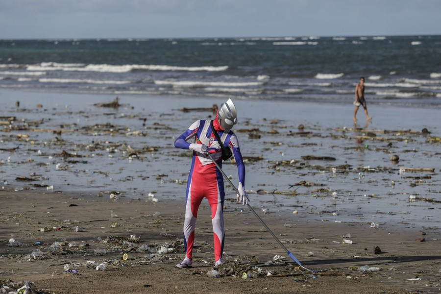 A person wears an Ultraman costume while raking trash on a beach.