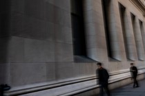A blurry color photograph of a couple men walking down Wall Street.