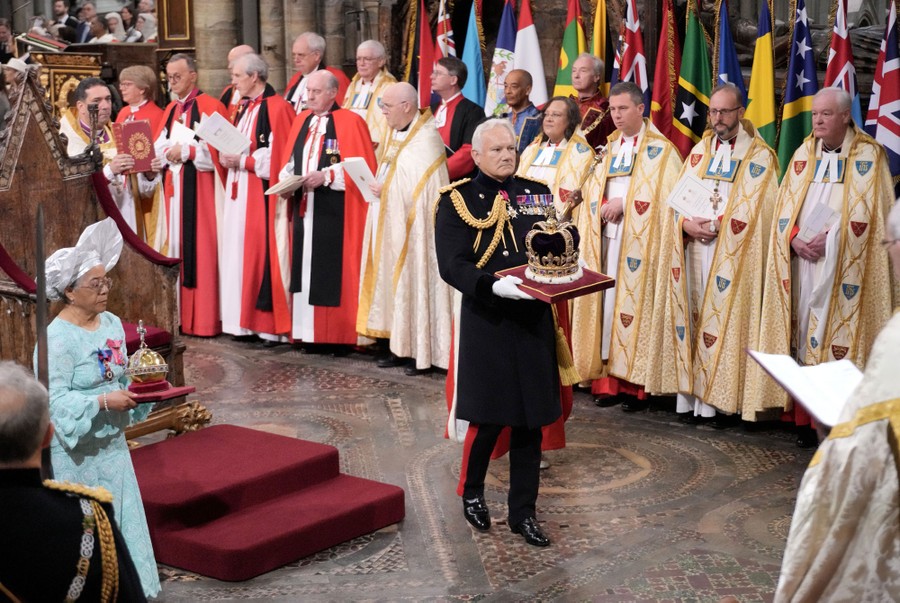A man in a military dress uniform carries the crown of the King of England