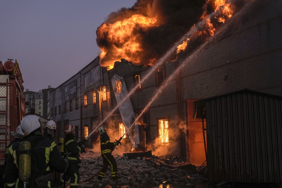 Firefighters stand outside a burning three-story building spraying water into the flames.