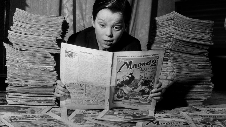 A black-and-white photo of a boy wearing a black shirt and peering at a newspaper comic, with newspapers stacked on both sides