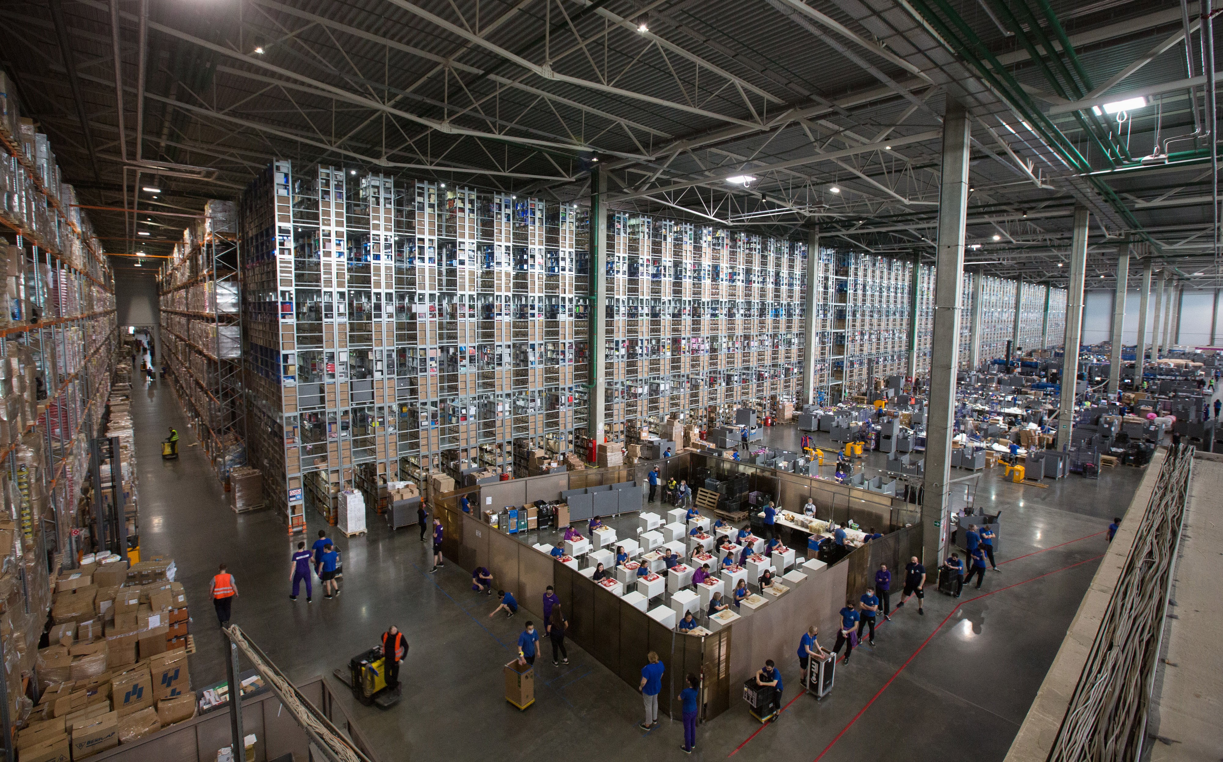 The vast interior of an online retailer's warehouse, filled with tall stacks of shelves and goods.