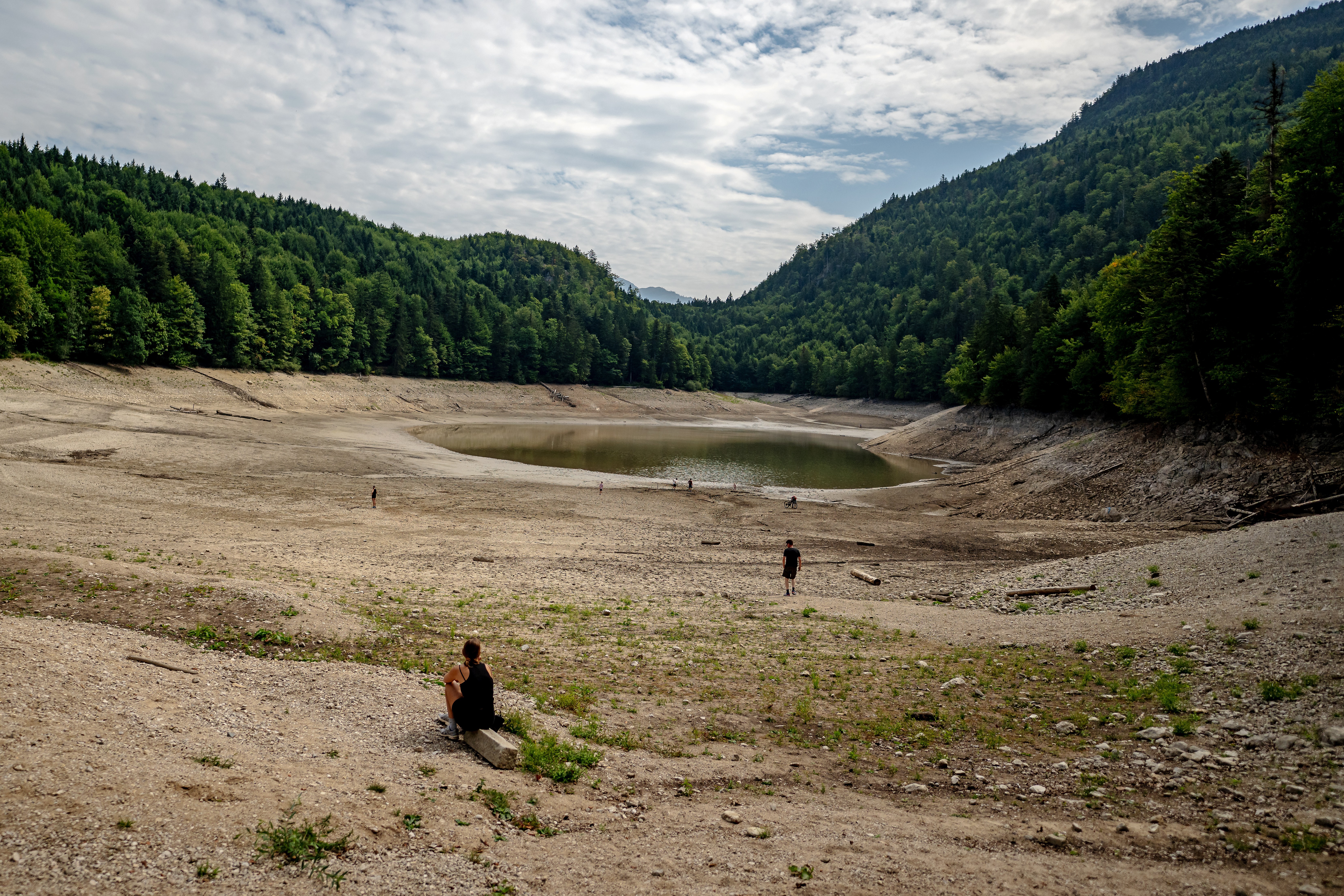 People walk along the exposed bottom of a drying mountain lake.